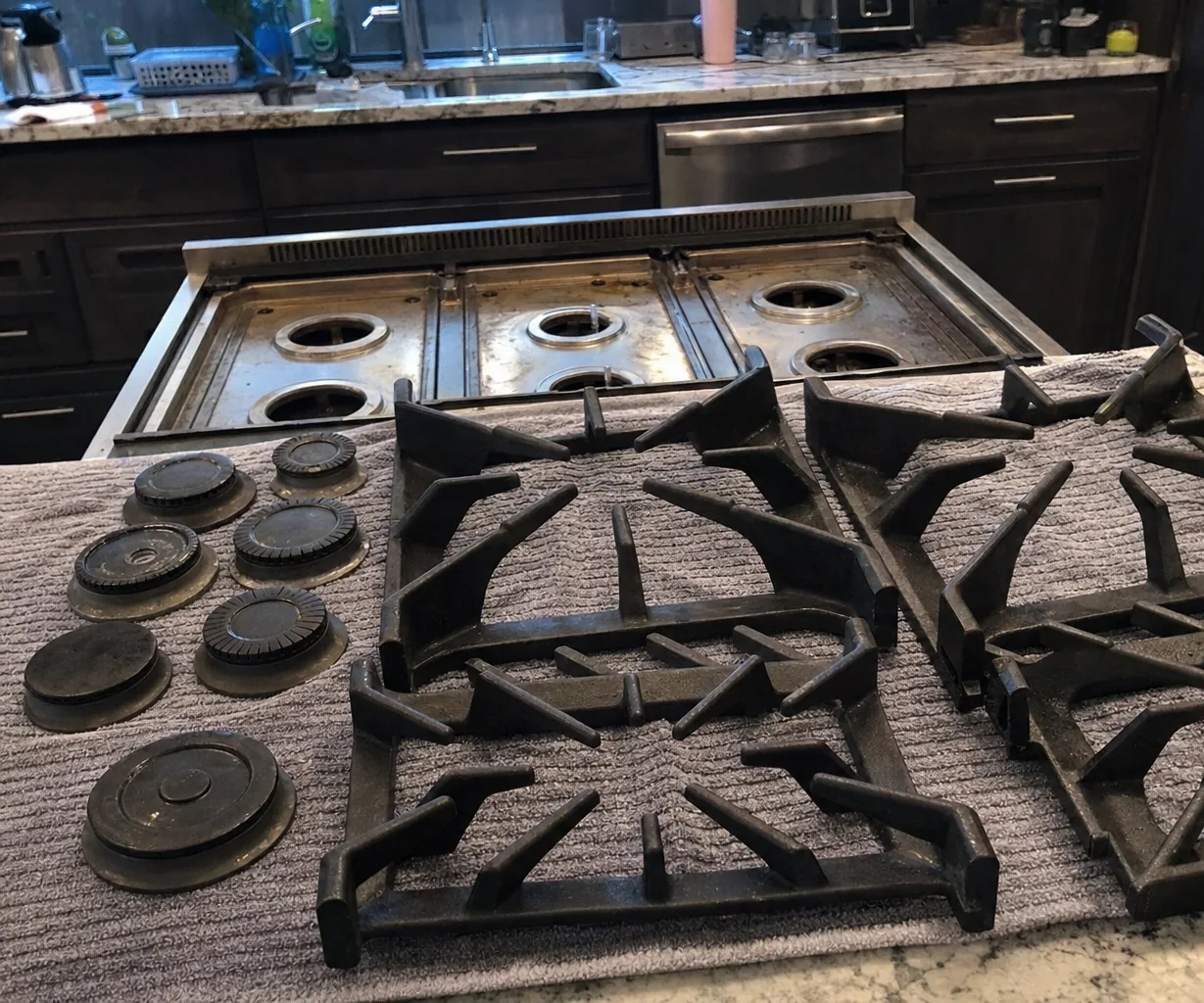 The back of a stripped rangetop and the counter behind it, grates drying on a towel in the foreground