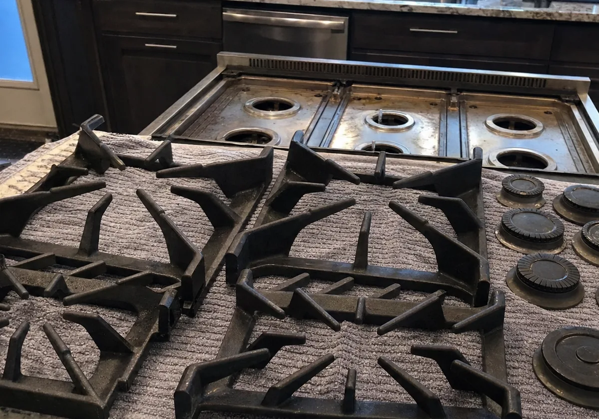 Cast grates and burner caps arranged on a towel beside an opened rangetop, everything laid out in order